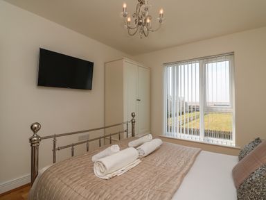 A bedroom with a bed with rolled towels a wall-mounted TV a wardrobe and a window with vertical blinds at Jurassic Coast House in Portland