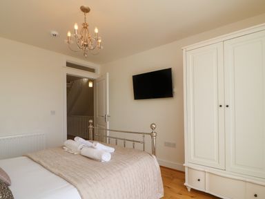 A bedroom with a metal bed frame and beige bedding with rolled white towels on the bed a white wardrobe a wall-mounted TV and a chandelier at Jurassic Coast House in Portland