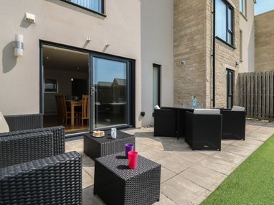 An outdoor patio with black wicker furniture including chairs and tables and sliding glass doors leading to a dining area at Jurassic Coast House in Portland