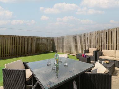 An outdoor patio area with a glass table, chairs, seating, and wooden fence at Jurassic Coast House in Portland