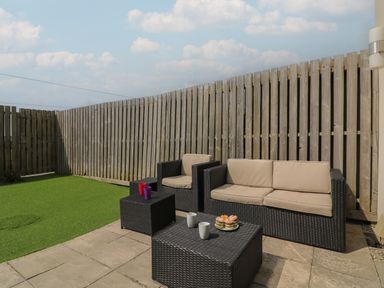 An outdoor patio with rattan sofa and chairs with cushions and a table with cups and cupcakes at Jurassic Coast House in Portland