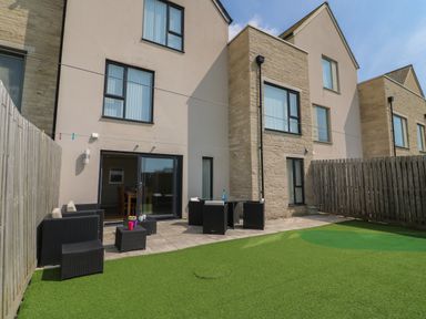 A fenced backyard with patio furniture and green artificial grass at Jurassic Coast House in Portland