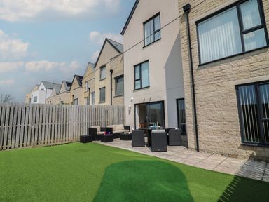 A patio with outdoor furniture and artificial grass next to a row of houses at Jurassic Coast House in Portland