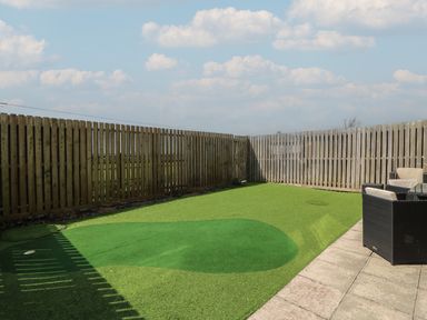 An outdoor area with artificial grass and a wooden fence with a patio and garden chairs Jurassic Coast House Portland