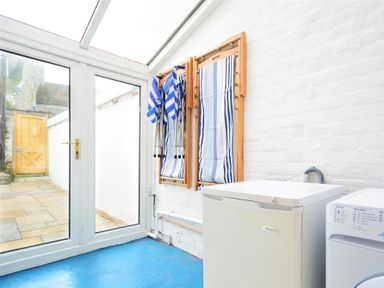 A utility room with a washing machine and drying racks on the wall with glass doors leading to a patio at Langham Cottage in Portland