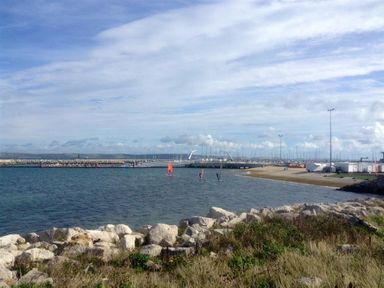 A coastal scene with windsurfers in the water and a marina with boats in the background at Langham Cottage in Portland