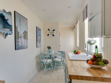 A kitchen with a wooden countertop a bowl of fruit a sink a small dining table with four chairs and wall art at Langham Cottage in Portland