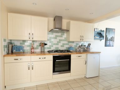 A kitchen with cream cabinets a gas stove a blue kettle a toaster and a small fridge at Langham Cottage in Portland
