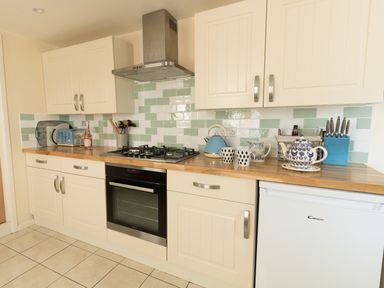 A kitchen with cream cabinets a gas stove an oven a blue kettle cups a blue toaster and a white fridge at Langham Cottage in Portland