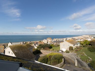 A coastal village with houses and gardens overlooking the sea on a clear day at Langham Cottage in Portland