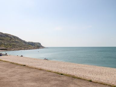 A pebble beach with a few people and umbrellas near the calm sea and cliffs at Langham Cottage in Portland