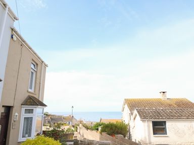 A view of houses and a garden wall overlooking the sea under a blue sky at Langham Cottage in Portland