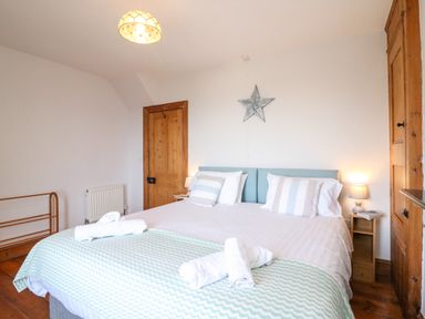 A bedroom with a double bed with striped pillows and rolled towels a wooden door and wardrobe and a star decoration on the wall at Langham Cottage in Portland