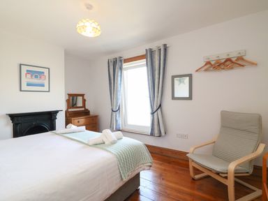 A bedroom with a bed, wooden dresser, armchair, window with curtains and coat hangers at Langham Cottage in Portland