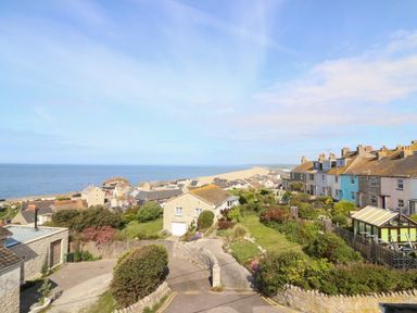 Houses on a hillside overlooking the sea and a sandy beach at Langham Cottage in Portland