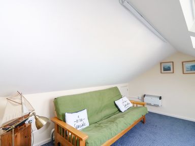 A room with a green sofa bed two cushions a wooden side table with a lamp and model sailboat and framed pictures on the wall at Langham Cottage in Portland
