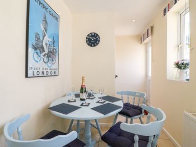 A dining area with a round table and four chairs a poster on the wall and a clock at Langham Cottage in Portland