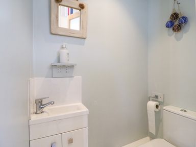 A small bathroom with a sink and faucet a wooden framed mirror above a soap dispenser a toilet with a roll of toilet paper on the wall and decorative balls hanging at Langham Cottage Portland