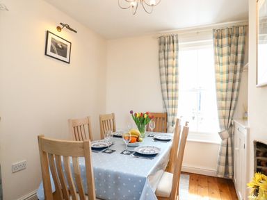 A dining room with a table set with plates glasses and a vase of flowers by a window with checked curtains at Langham Cottage Portland