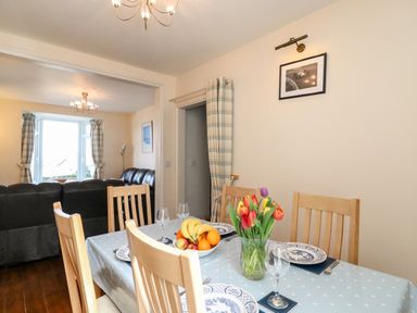 A dining room with a table set with plates glasses and a vase of flowers next to a living room with sofas at Langham Cottage in Portland