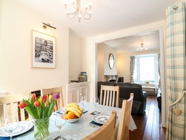 A dining area with a wooden table set with plates and glasses next to a living room with leather sofas at Langham Cottage in Portland