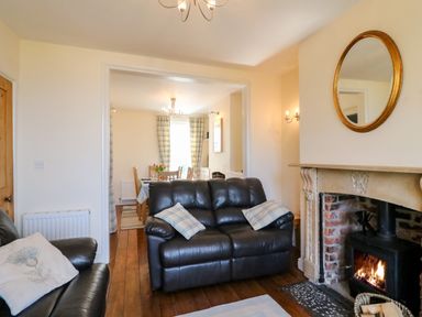 A living room with leather sofas and a fireplace opening to a dining area with a table and chairs at Langham Cottage Portland