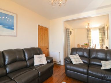 A living room with two dark leather sofas and cushions with a dining area visible through a doorway at Langham Cottage in Portland