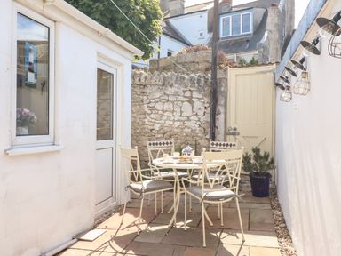 An outdoor patio with a round table and four chairs next to a white building and stone wall at Langham Cottage in Portland