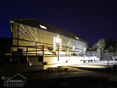 A stone cottage with a wooden railing and exterior lights at night at Leys At Valley View Farm in Uplyme