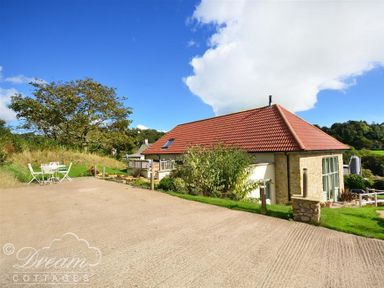 A stone cottage with a red tiled roof and outdoor seating area surrounded by grass and trees at Leys At Valley View Farm in Uplyme