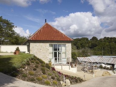 A small stone building with a red tiled roof and garden on a slope at Leys At Valley View Farm in Uplyme