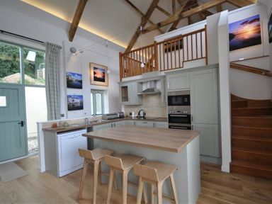 A kitchen with wooden stools and a breakfast bar under wooden beams with a staircase at Leys At Valley View Farm in Uplyme
