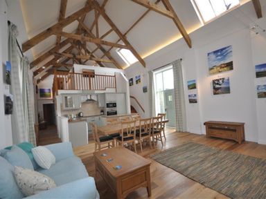 An open living room and kitchen with wooden beams dining table sofa and picture frames on walls at Leys At Valley View Farm in Uplyme