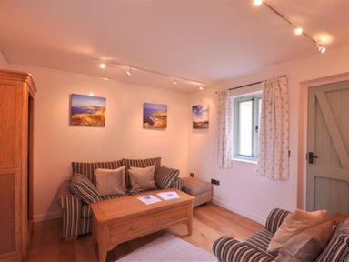 A sitting room with striped sofas wooden coffee table wooden cabinet and landscape pictures on the wall at Leys At Valley View Farm in Uplyme