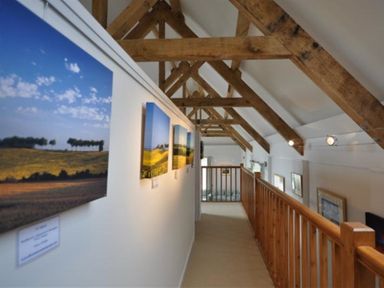 A hallway with wooden beams and framed landscape photos on the wall at Leys At Valley View Farm in Uplyme