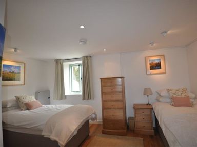 A bedroom with a double bed and a single bed with wooden drawers and nightstand at Leys At Valley View Farm in Uplyme