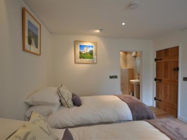 A bedroom with two beds pillows and blankets a wooden door and a small bathroom visible through an open door at Leys At Valley View Farm in Uplyme