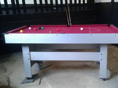 A pool table with a red playing surface and pool balls on it in a room with dark walls