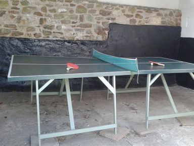 A ping pong table with paddles and a ball in a room with stone and black walls at Leys At Valley View Farm in Uplyme