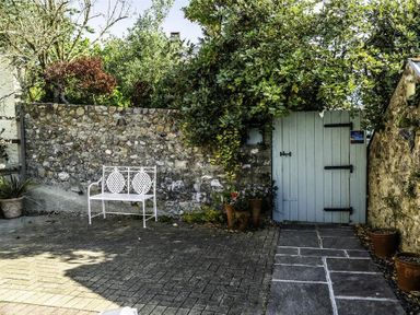 An outdoor stone paved area with a white metal bench a stone wall green foliage and a light blue wooden gate at Leys At Valley View Farm in Uplyme