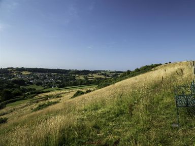A grassy hillside with a view of a village and fields under a clear sky at Leys At Valley View Farm in Uplyme
