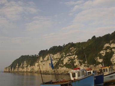 Boats moored near white chalk cliffs with greenery under a cloudy sky