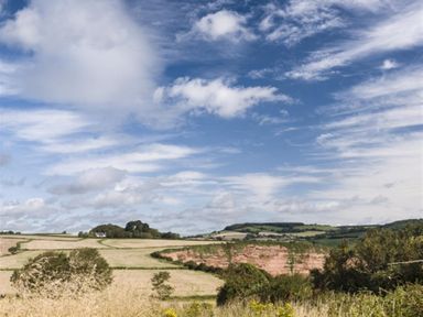 A rural landscape with fields bushes and hills under a blue sky with clouds at Leys At Valley View Farm in Uplyme
