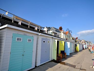 A row of beach huts with different colored doors along a paved walkway with houses and street lamps in the background at Leys At Valley View Farm in Uplyme