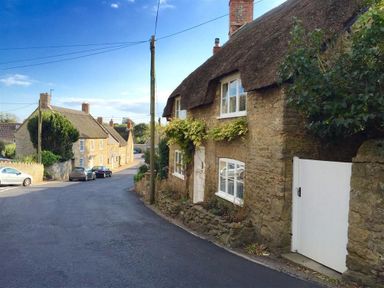 A street with stone cottages and cars parked along the road at Lilac Cottage in Burton Bradstock