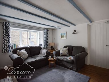 A sitting room with two grey sofas a small wooden table with cups and snacks and blue patterned curtains at Lilac Cottage in Burton Bradstock