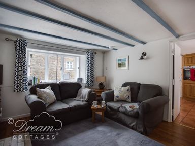 A living room with two sofas a window with patterned curtains and a view of an adjoining kitchen at Lilac Cottage in Burton Bradstock
