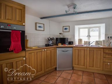A kitchen with wooden cabinets a dishwasher an oven and a window at Lilac Cottage in Burton Bradstock