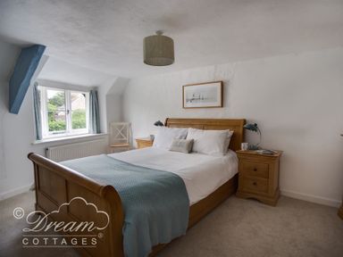 A bedroom with a wooden bed blue throw and bedside tables at Lilac Cottage in Burton Bradstock