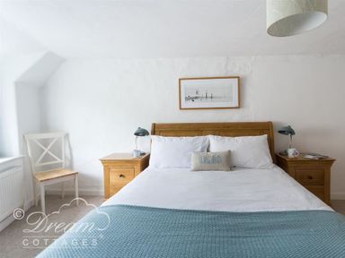 A bedroom with a wooden bed with white bedding and blue throw blanket with wooden bedside tables and lamps at Lilac Cottage Burton Bradstock